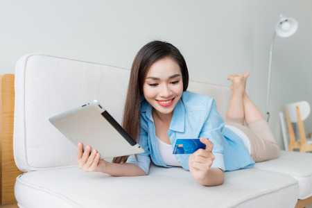 Woman shopping on tablet computer and credit card sitting in sofa smiling happyの写真素材