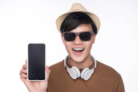 Smart casual asian man seated on chair, showing smartphone screen in studio backgroundの写真素材