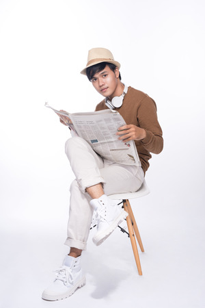 Smart casual asian man seated on chair, reading newspaper in studio backgroundの写真素材