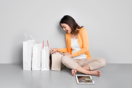 Young asian woman shopping online at home sitting besides row of shopping bagsの写真素材