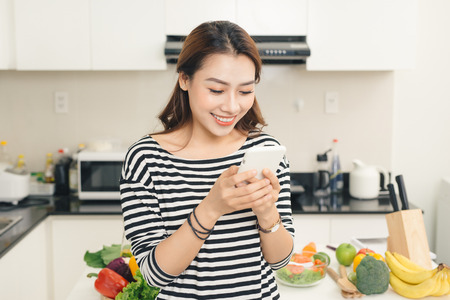 Smiling asian woman in the kitchen writing text messageの写真素材
