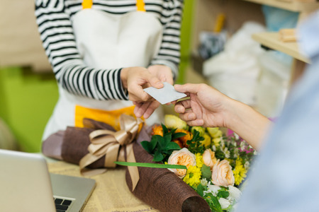 Young woman working as florist giving credit card to customerの写真素材