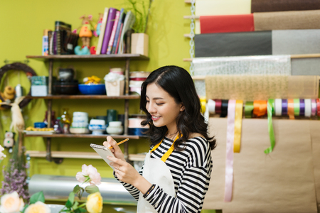 Smiling asian female florist making notes at flower shop counterの写真素材
