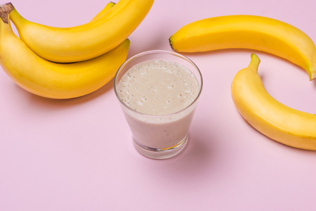Fresh made banana smoothie in a glass on pink backgroundの写真素材