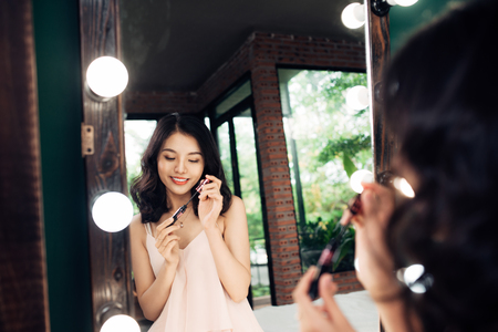 Portrait of beautiful young woman looking at the mirror applying black mascara on eyelashes at homeの写真素材