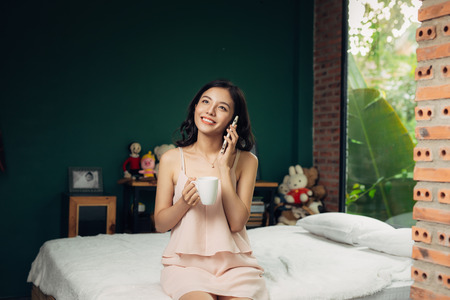 Pretty vietnamese woman enjoying her morning talking to mobile phoneの写真素材
