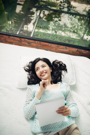 Author, Typewriter, Journalist. Intelligent woman lying on bed and thinkingの写真素材