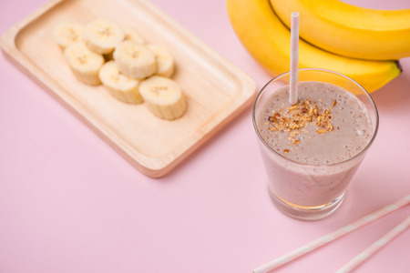 Fresh made banana smoothie in a glass on pink backgroundの写真素材