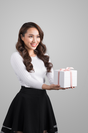 Portrait of a smiling pretty asian woman holding gift box isolated over gray backgroundの写真素材