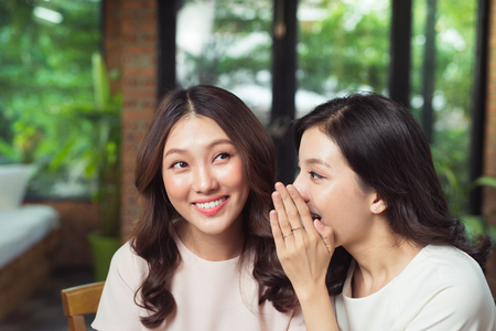 Two girls gossiping. Attractive young woman whispering secret in friend's earの写真素材