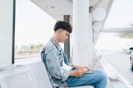 Asian young man sitting on the chair at the airport payment using credit card and laptop.の写真素材