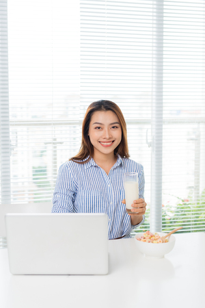 Young attractive asian businesswoman drinking milk while sitting at office deskの写真素材