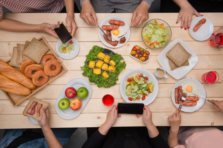 Group of happy smiling friends with smartphones taking picture of foodの写真素材