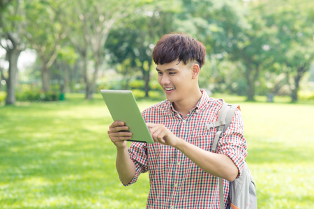 Male asian student using digital tablet in parkの写真素材