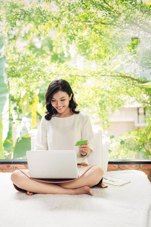 Beautiful asian womon holding a credit card and purchasing onlineの写真素材