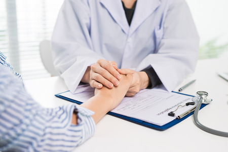 Female doctor in white medical coat doctor and patient sitting at the desk near the window in hospitalの写真素材