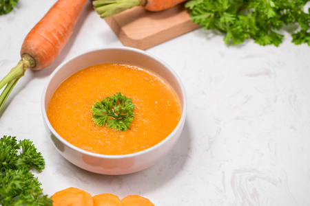 Carrot soup with cream and parsley on white stone background. Top view. Copy spaceの写真素材