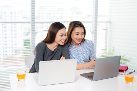 Two young business women sitting at table holding digital tableの写真素材