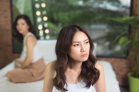 Two friends not talking to each other after fight on bed in sitting room at homeの写真素材