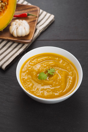 Pumpkin soup in a bowl with fresh pumpkins, garlic and parsley herbsの写真素材