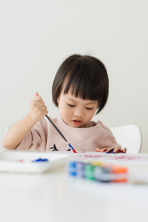 Little asian girl painting with paintbrush and colorful paintsの写真素材