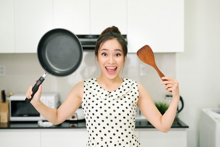 Happy housewife hold up with pan wooden turner in kitchenの写真素材