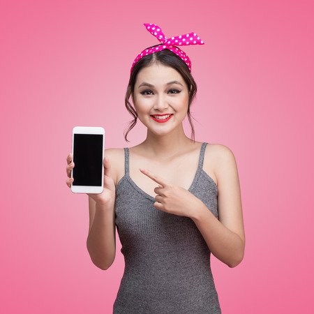 Beautiful young asian woman with pin-up make-up and hairstyle over pink background with mobile phoneの写真素材