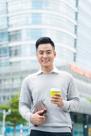 Portrait of a handsome man standing with coffee on city streetの写真素材