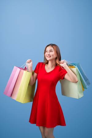 Beautiful young asian woman with colored shopping bags over blue backgroundの写真素材