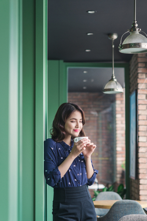 Portrait of happy young business woman with mug in hands drinking coffee in the morning at restaurantの写真素材