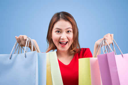 Beautiful young asian woman with colored shopping bags over blue backgroundの写真素材