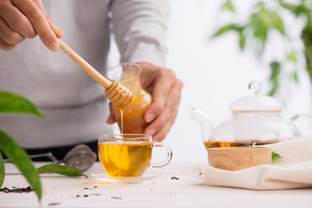 Cropped image of arista pouring honey into cup of teaの写真素材
