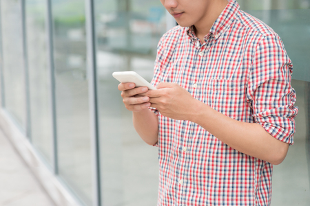 Happy asian man smiling as he reads a text message standing outside the officeの写真素材