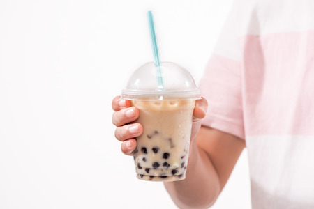 Drinking light brown creamy bubble tea and black tapioca pearls in plastic cups on table.の写真素材