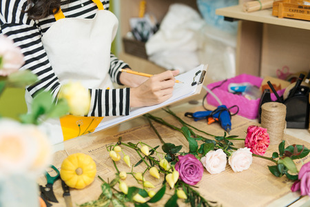 Smiling asian female florist making notes at flower shop counterの写真素材