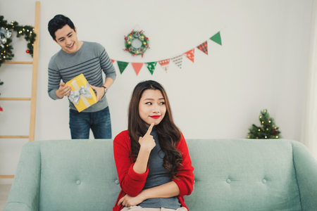 Christmas Asian Couple. A handsome man giving her girlfriend/wife a gift at home celebrating New Year Peopleの写真素材