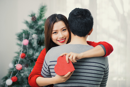 Christmas Asian Couple. A handsome man giving her girlfriend/wife a gift at home celebrating New Year Peopleの写真素材