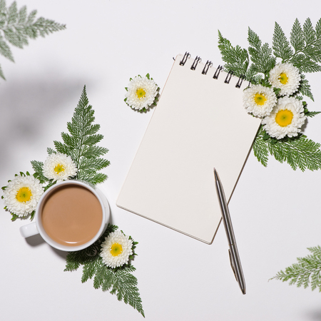 Flat lay of green leaves and flowers pattern with cup of coffee and paper note on white backgroundの写真素材