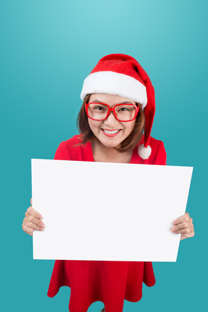High view of smiling beautiful happy girl in christmas santa hat holding blank board on blue background.の写真素材