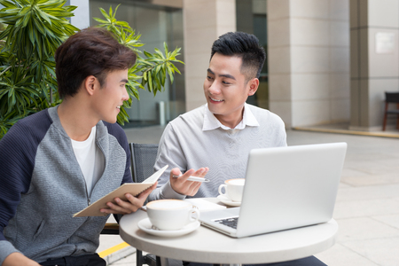 Handsome Asian business colleagues or college students work together using laptop, startup project meeting or teamwork brainstorm concept, at coffee shop or modern officeの写真素材