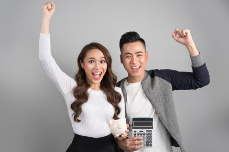 Young couple hold pink pig bank and calculator standing over on gray backgroundの写真素材