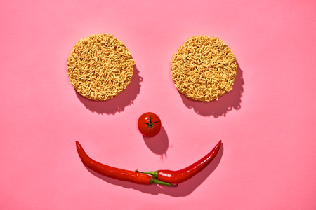 Food concept. face made of hot chilli, tomatos, noodle on pink backgroundの写真素材