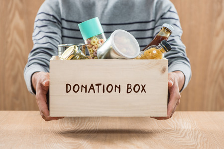 Volunteer with donation box with food stuffs on wooden backgroundの写真素材