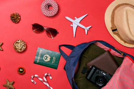 Preparation for travel concept - passport, camera, hat, airplane, chrismas decorations on red backgroundの写真素材