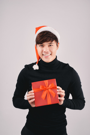 Young handsome asian man with santa hat holding a gift, isolatedの写真素材