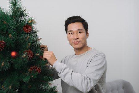 Celebrating New Year. Asian man standing by new christmas tree at home の写真素材