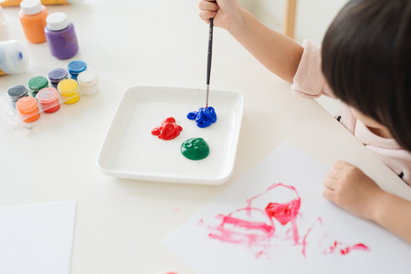 Little asian girl painting with paintbrush and colorful paintsの写真素材