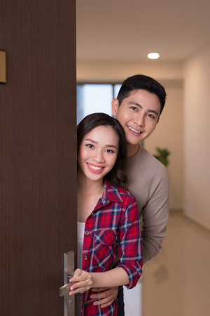 Cheerful young asian couple inviting people to enter in homeの写真素材