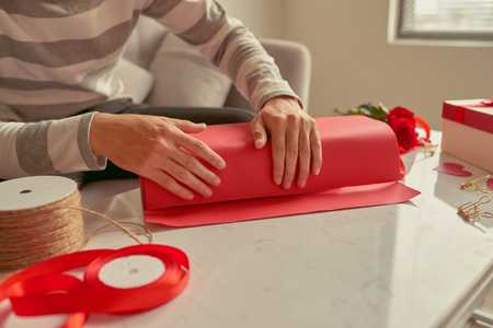 A man wrapping gifts  in red ribbon and fresh roses. Valentines conceptの写真素材