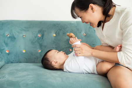 Mother and baby daughter plays, hugging, kissing at home on the couch